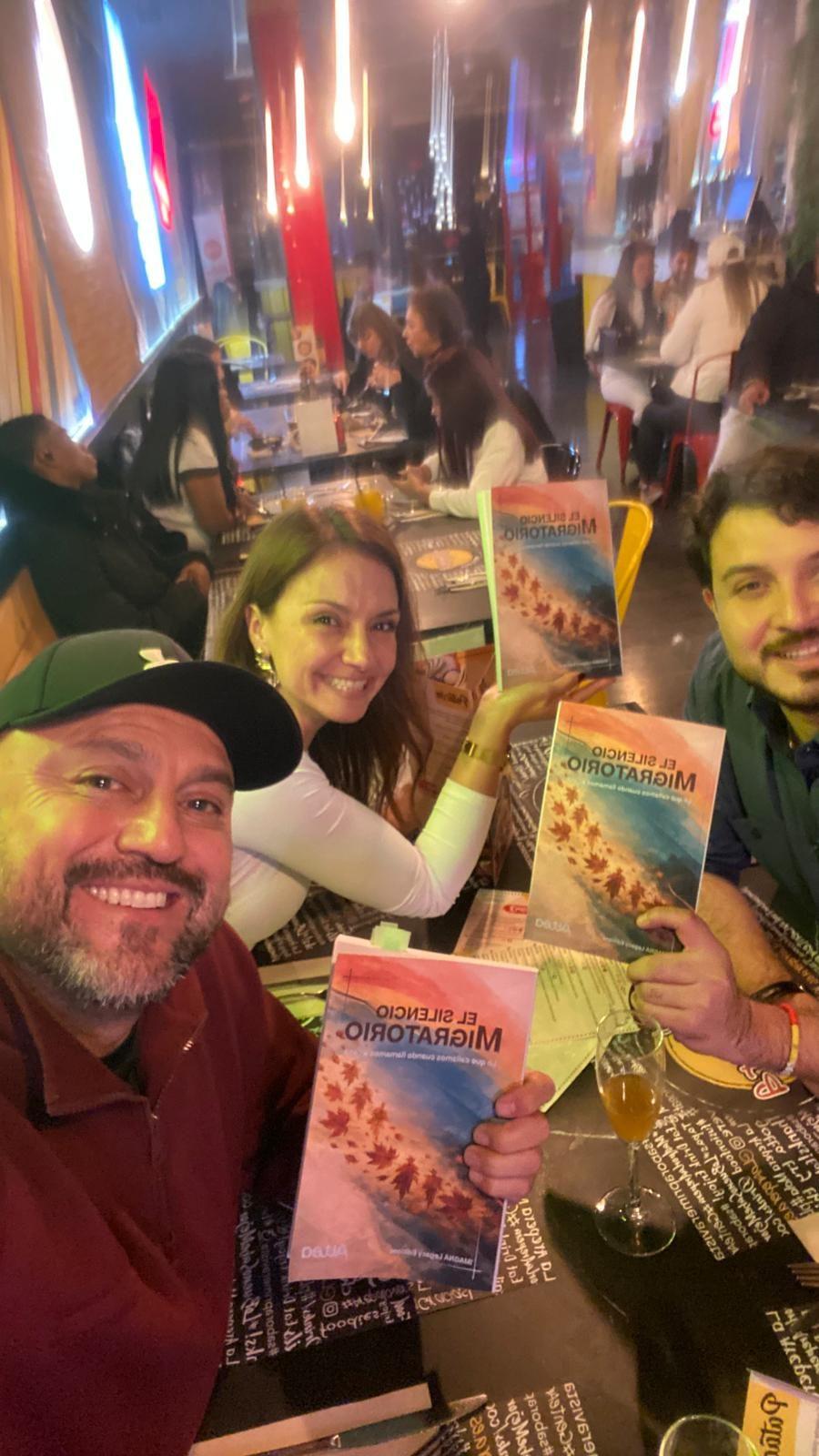 Selfie en un restaurante con miembros de la comunidad sosteniendo el libro